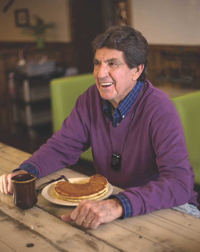 A man sitting at a table with pancakes and coffee.